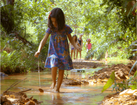 Girl in the middle of nature playing with a tree leaf while going through a puddle